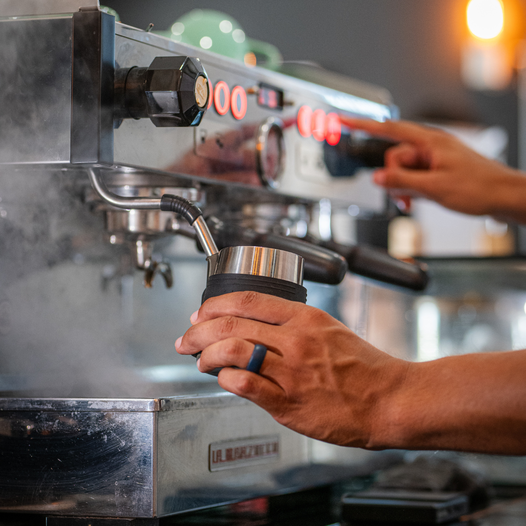 Espresso machine with Barista steaming milk in milk pitcher while making espresso