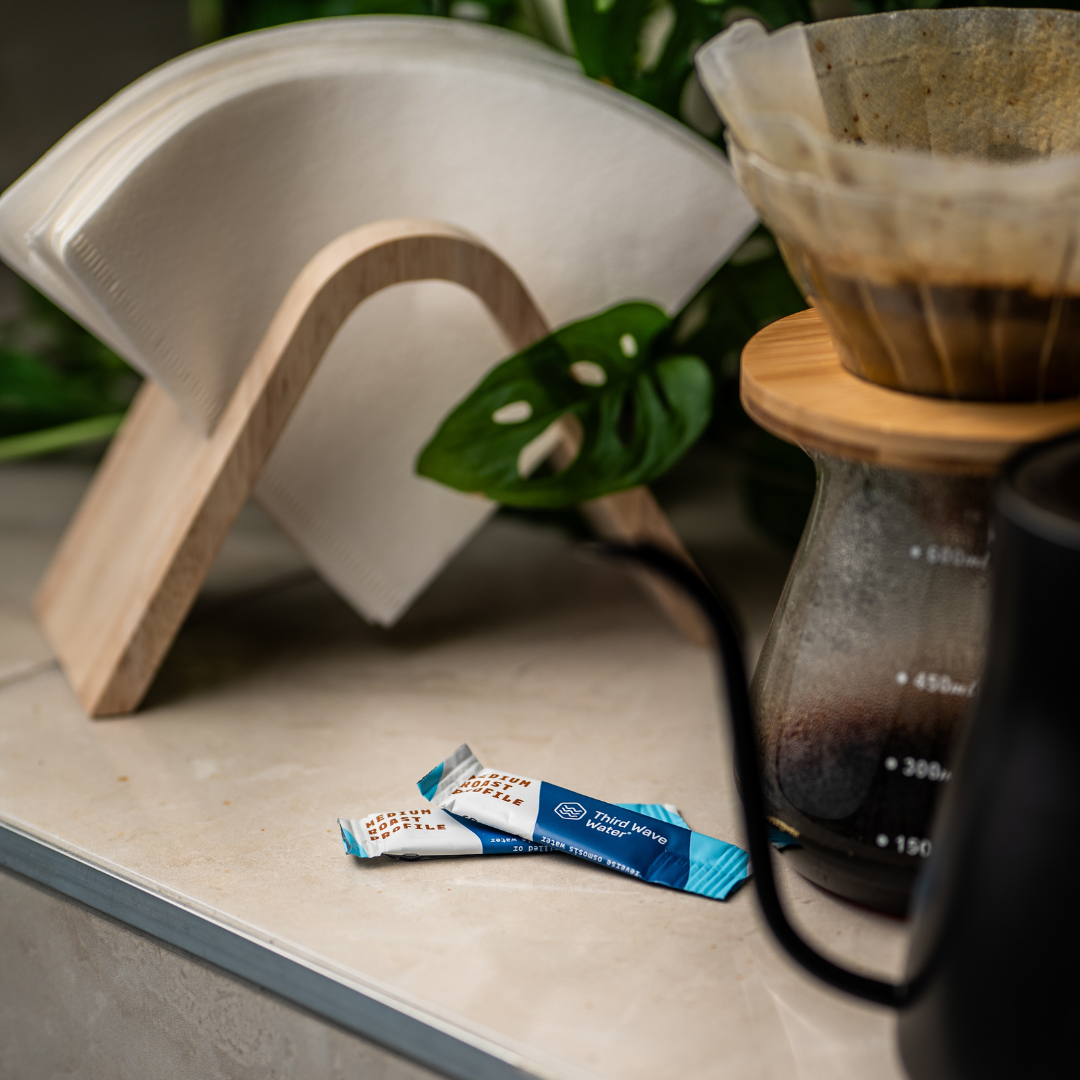 Pour over filter coffee being brewed with a third wave water sachet in foreground with paper coffee filters in a filter stand holder.